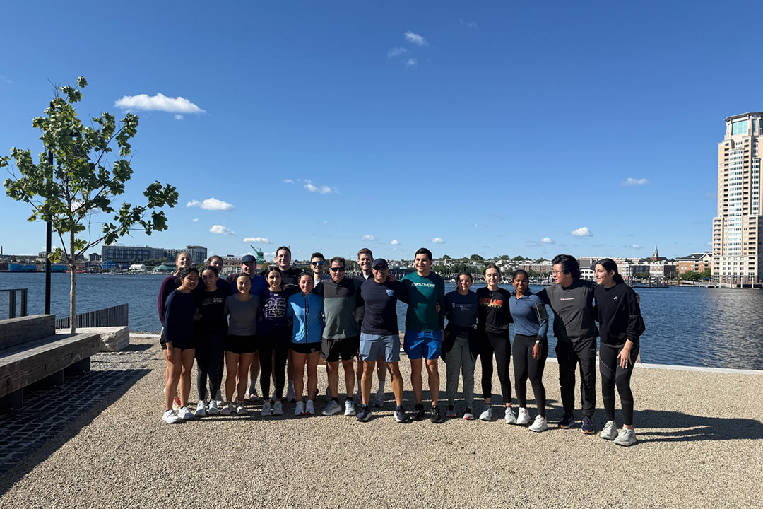 Dean Gladwin and Dr. Shah join the UMSOM run club and pose for a group photo along Baltimore's Inner Harbor on a sunny day.